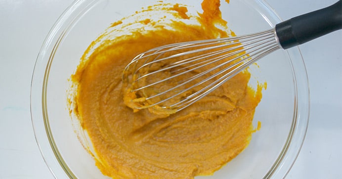 A whisk in a bowl a pumpkin.