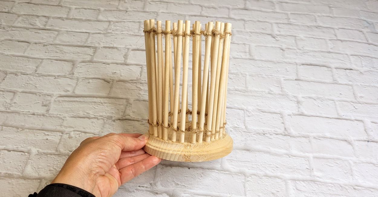 A hand holding a craft with dowel rods on a wooden base